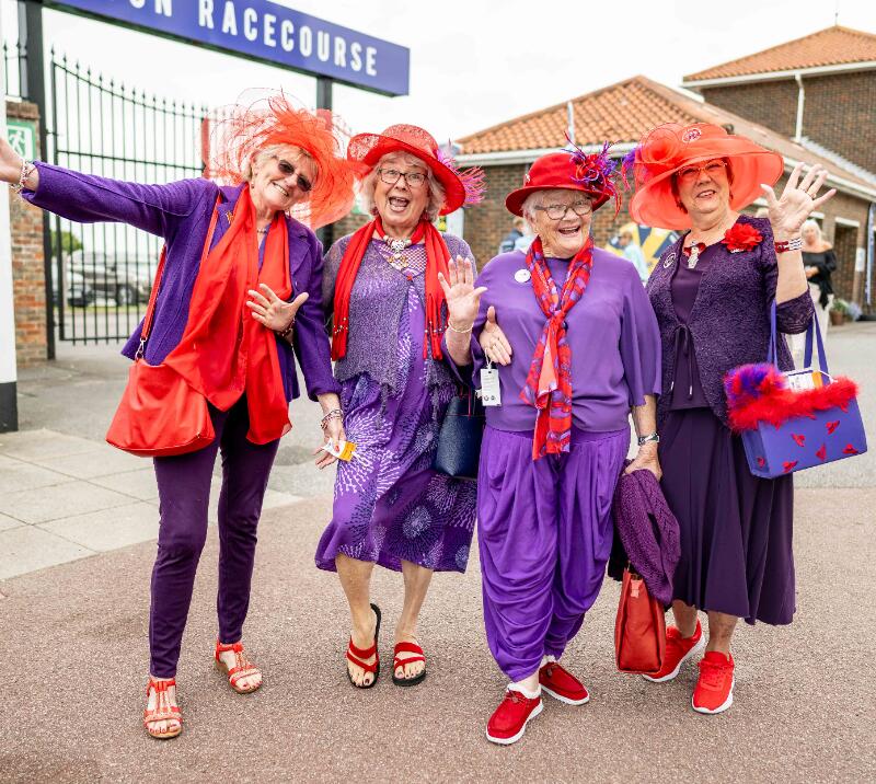 A group of very happy ladies dressed in purple and red in front of Brighton Racecourse
