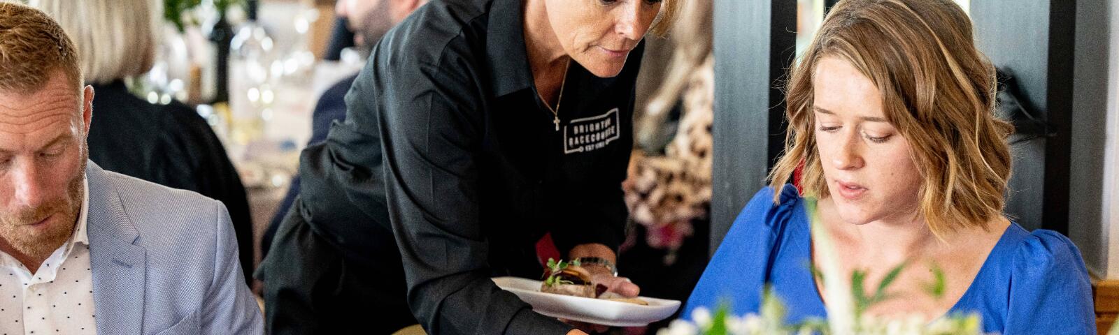 A member of waiting staff serving food to hospitality guests at Brighton Racecourse
