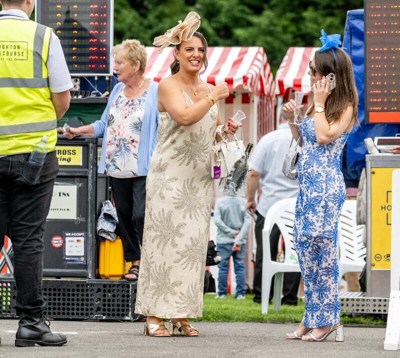 Two ladies dressed for the races in front of the betting boards at Brighton