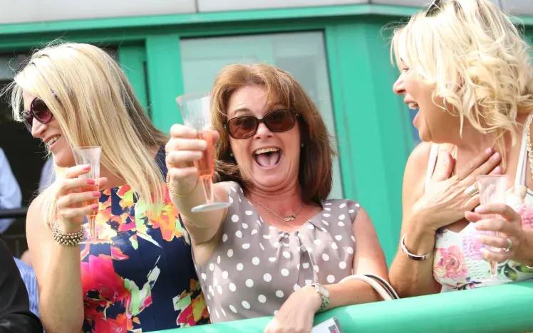 Three women on the hopsitality balcony at Brighton Racecourse cheers their glasses happily